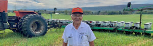 Elderly man smiles in front of his tractor and field