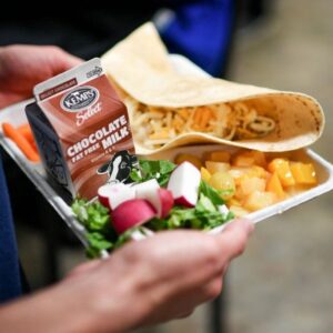 Person carrying lunch tray that has salad, fruit, tacos and chocolate milk
