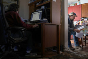Man on computer and man at table reading papers